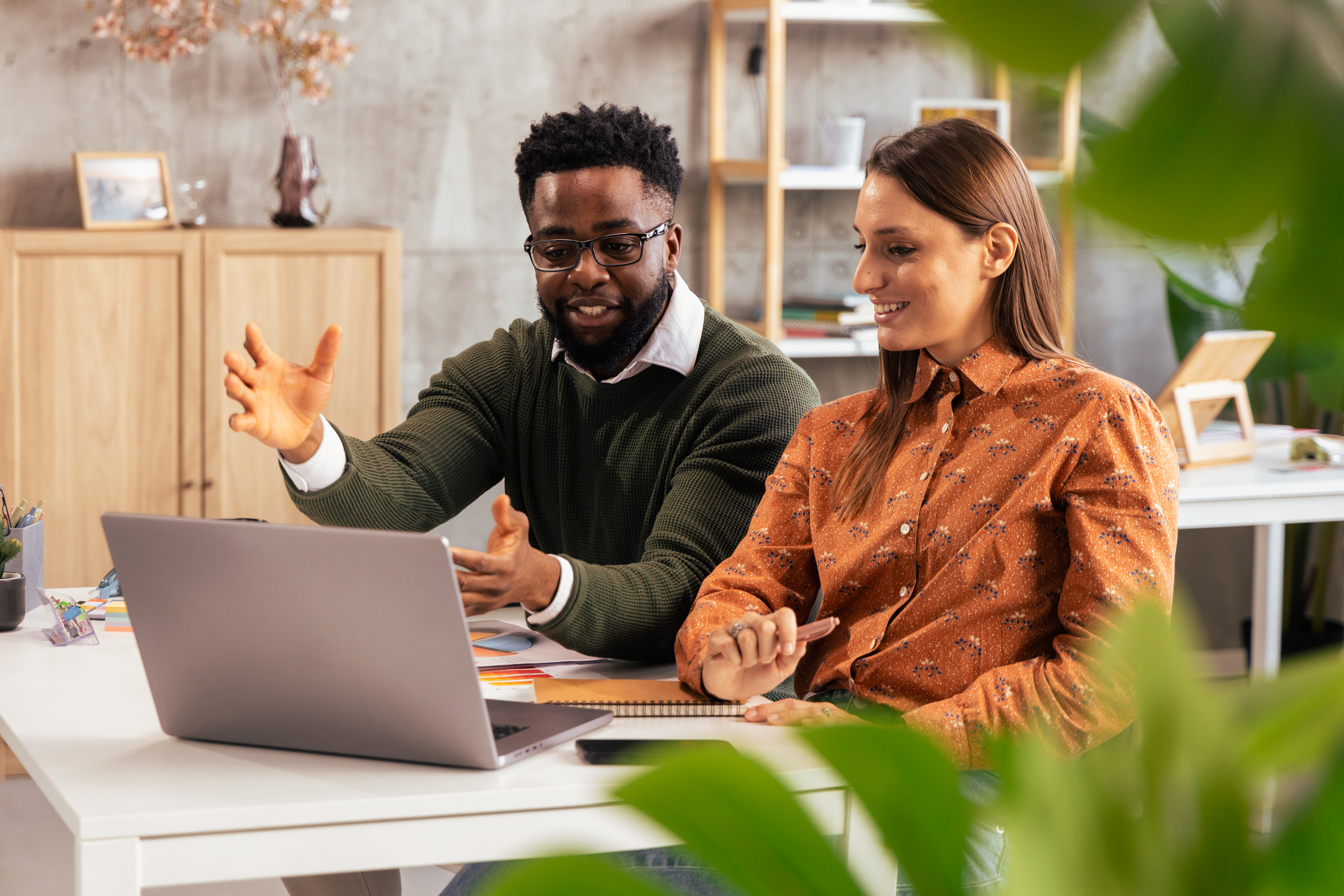 Ein Mann und eine Frau sitzen vor einem Laptop. Der Mann erklärt etwas