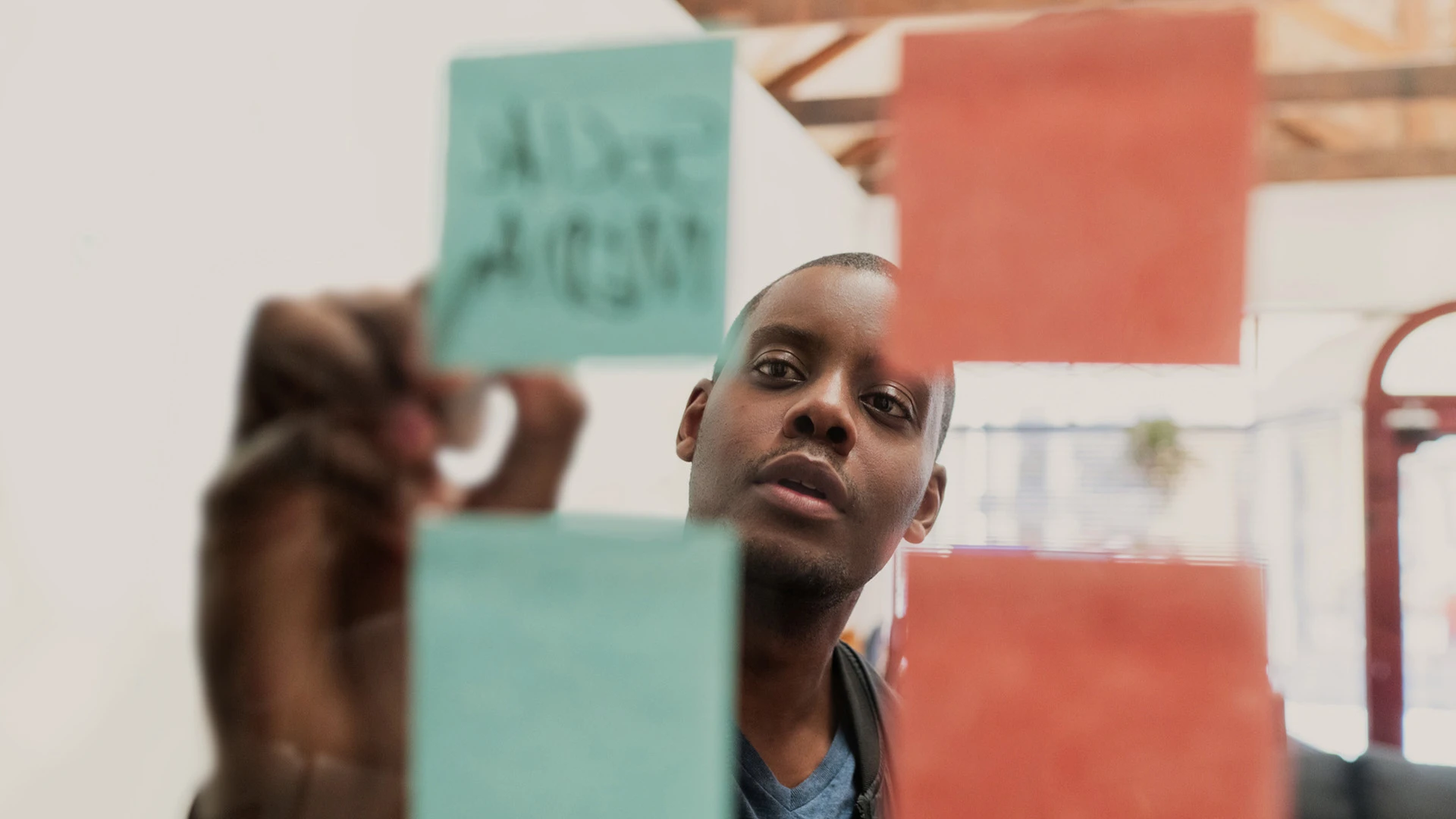 CloseUp eines Mannes, der etwas auf ein Post it schreibt, durch eine Glaswand fotografiert.