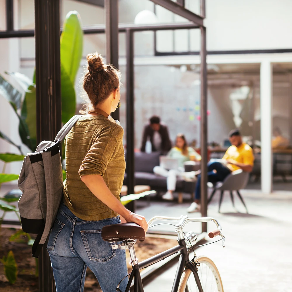 Frau in Rückansicht, die ihr Fahrrad Richtung Office schiebt