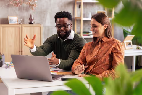 Ein Mann und eine Frau sitzen vor einem Laptop. Der Mann erklärt etwas