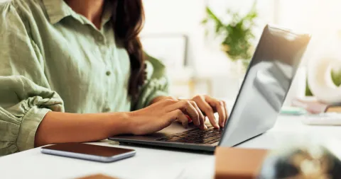 Großaufnahme von Frauenhänden die etwas auf einem Laptop tippen